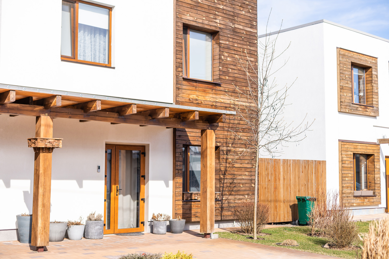 Außenansicht eines weißen Reihenhauses mit Vordacj aus Holz und einer braunen Haustür