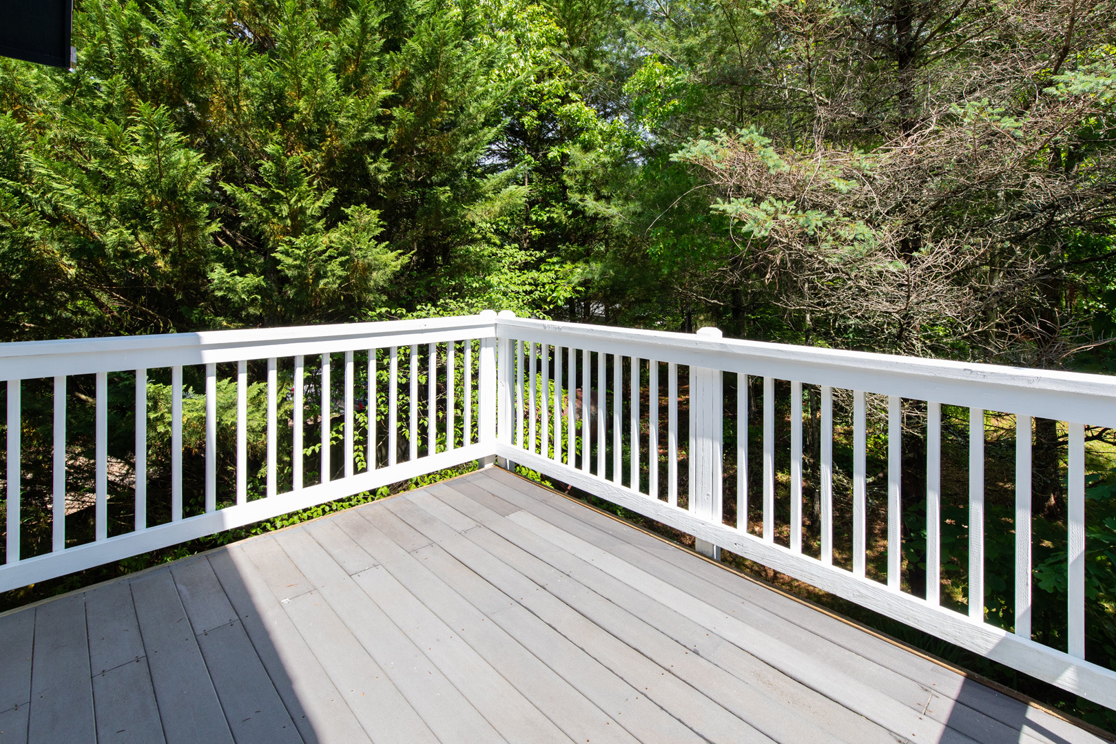 Balkon mit weißem Holzgeländer und Holzboden mit Blick in einen Wald