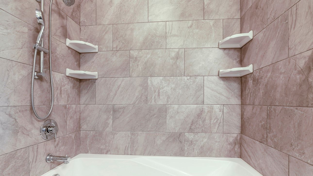 Badezimmeransicht mit gefliester Wand, moderner Duscharmatur, Handbrause und Badewanne.