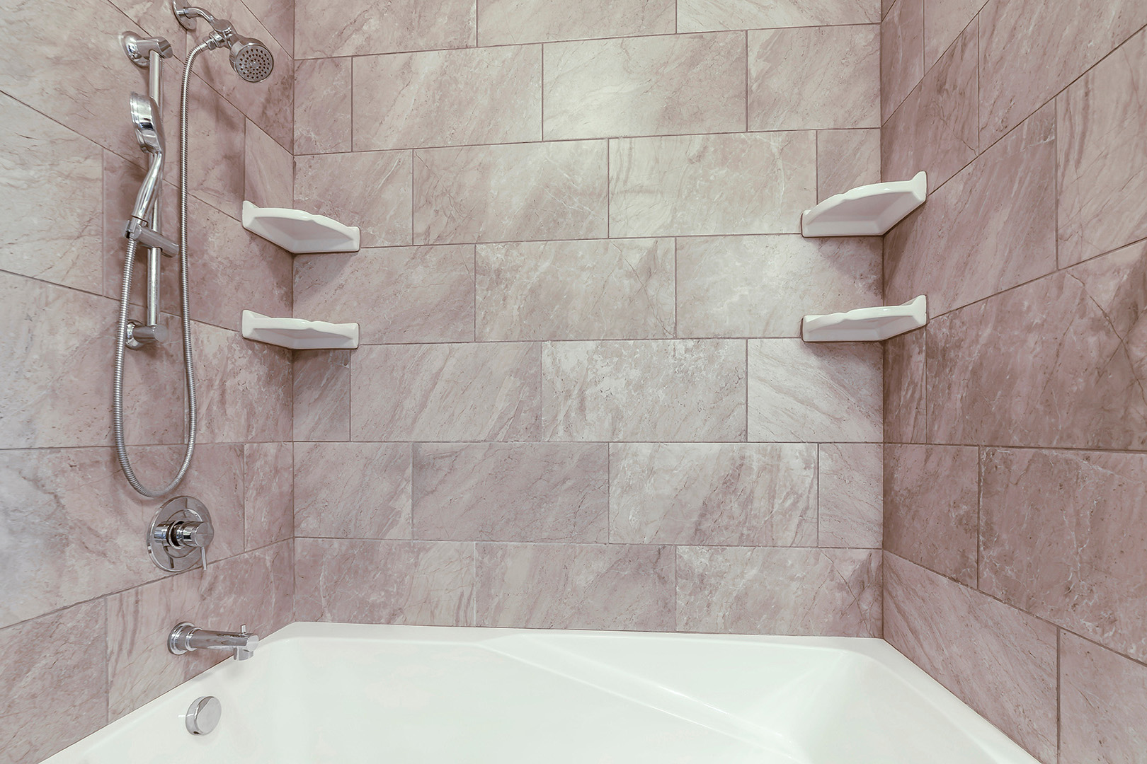 Badezimmeransicht mit gefliester Wand, moderner Duscharmatur, Handbrause und Badewanne.